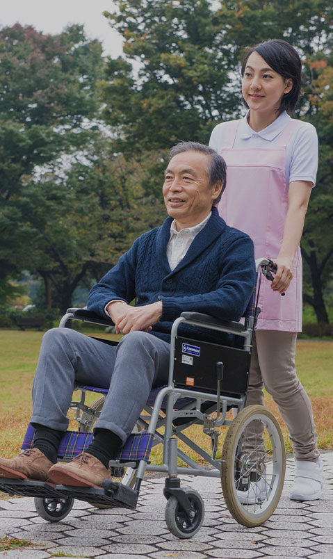 介護職員と入居者が庭で車椅子での散歩・憩いの時間を過ごしている様子